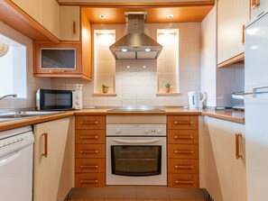 A compact kitchen with wooden cabinets, a built-in oven, a microwave, and a stainless steel range hood.