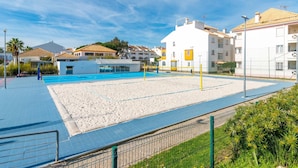 Ein Beachvolleyballfeld mit einem Pool, umgeben von Gebäuden mit Balkonen und einem klaren Himmel.