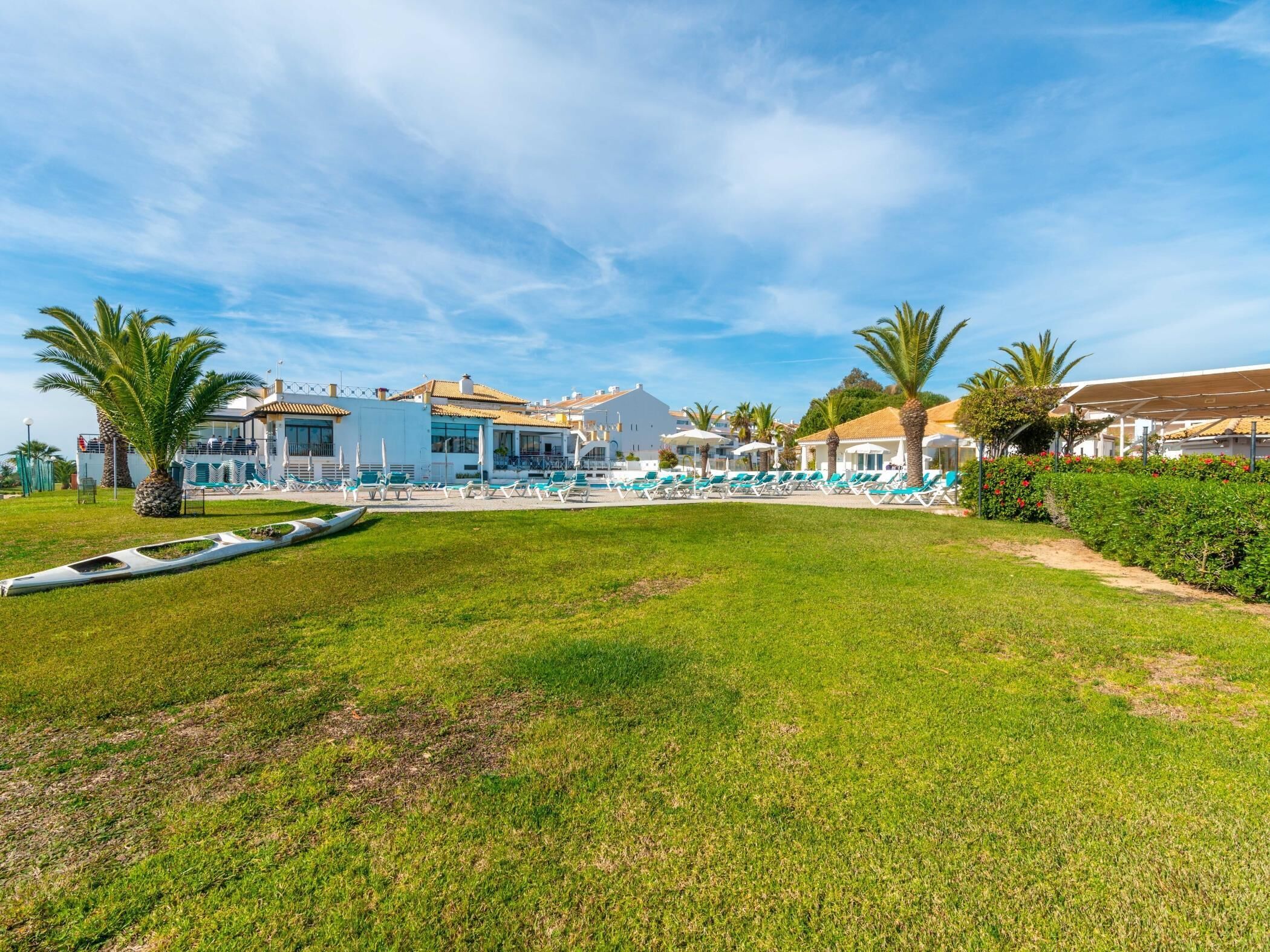 Un complexe hôtelier doté d’une piscine, de palmiers et d’une pelouse bien entretenue.