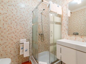 Un bagno con doccia vetrata, lavandino bianco e parete rivestita di piastrelle.