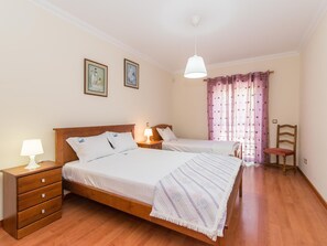 Un letto matrimoniale con testiera in legno, due comodini con lampade, una cassettiera in legno, una sedia e una finestra con tende viola.