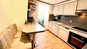 A compact kitchen with white cabinets, a built-in oven, and a dining area with a cushioned bench. - Antibes City Center – 4 Guests (Antibes)