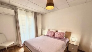 A bedroom with a bed, bedside tables, a chair, and a window with curtains. - Antibes City Center – 4 Guests (Antibes)