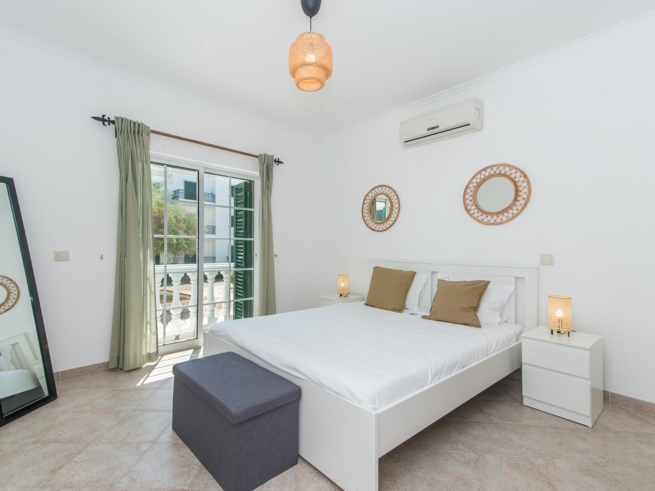 Ein Schlafzimmer mit einem Bett, Nachttischen, einer Bank, einem Fenster mit Vorhängen und Wandaircondition.