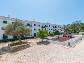 A courtyard with a playground, a tree, and a building with balconies. - Casa do Lagar - 4 mins walk to train station - quiet - wi-fi (Conceição de Tavira)