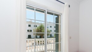 A room with a large sliding glass door leading to an outdoor area with a white balustrade and a building in the background. - Casa do Lagar - 4 mins walk to train station - quiet - wi-fi (Conceição de Tavira)