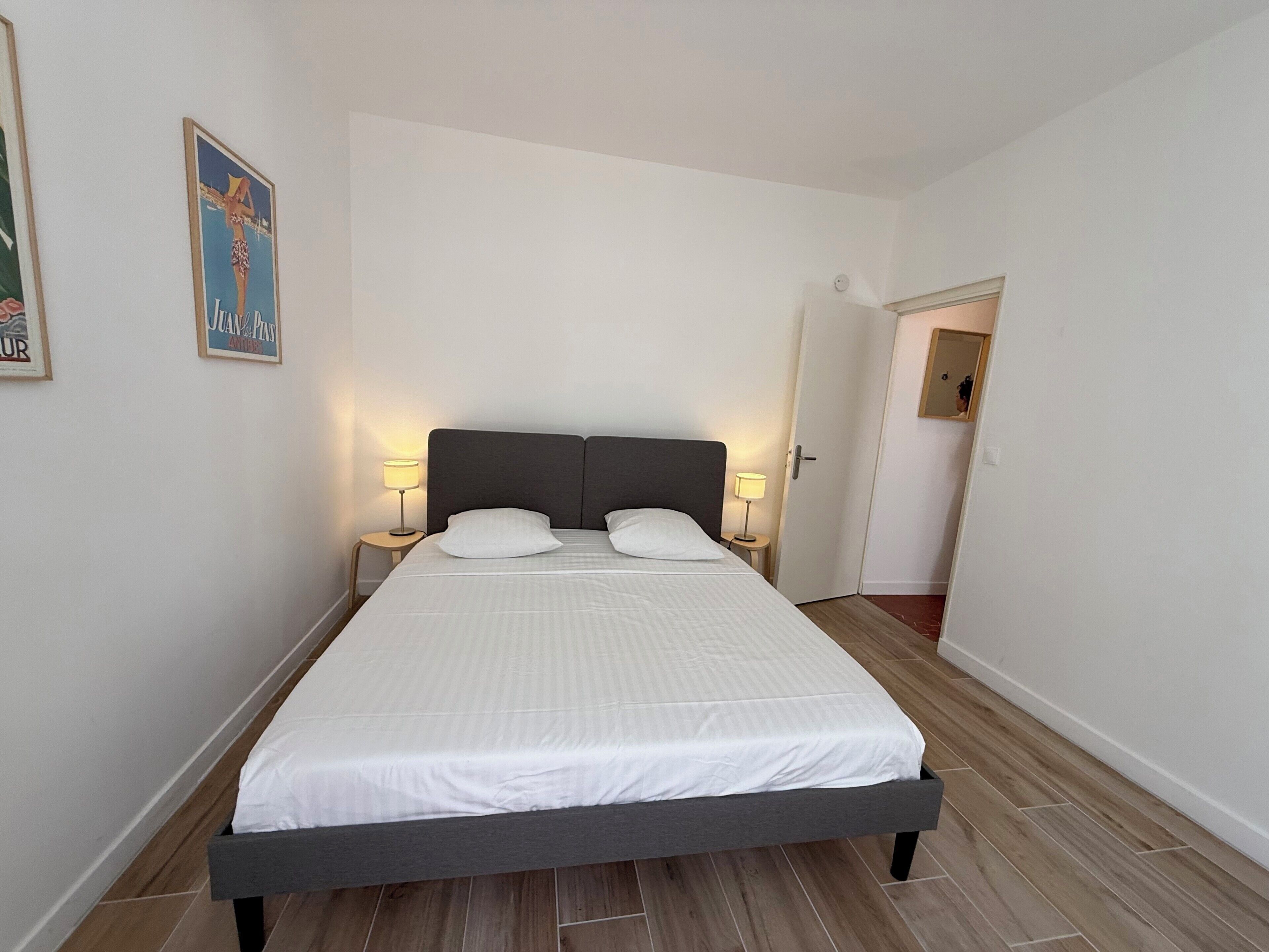Una cama bien hecha con un cabecero oscuro, dos lámparas de noche y un cuadro en la pared.