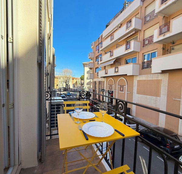 Un balcone con tavoli gialli apparecchiati per mangiare, che si affaccia su una strada con auto parcheggiate e palazzi.