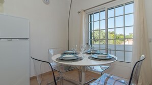 A dining area with a round table, chairs, and a window with a view. - Casa Oceanus - Magnificent Apartment with Pool (Cabanas de Tavira)