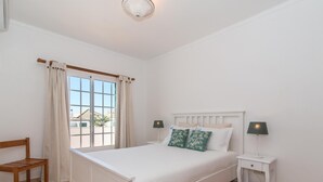 A bedroom with a bed, two bedside tables, a chair, and a window with curtains. - Casa Oceanus - Magnificent Apartment with Pool (Cabanas de Tavira)