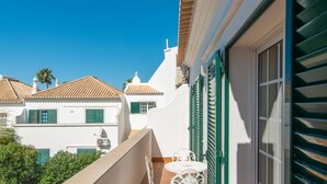 A balcony with a table and chairs, overlooking a street with traditional buildings and a clear blue sky. - Casa Oceanus - Magnificent Apartment with Pool (Cabanas de Tavira)