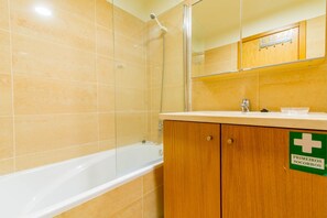 Een badkamer met een badkuip, een douche en een wastafel met spiegel. Op de wastafel staat een bordje met de tekst 'Primeiros Socorros' (Eerste Hulp).
