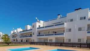 Un edificio moderno con diversi balconi, una piscina e un cielo azzurro limpido.