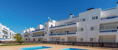 A modern apartment building with multiple balconies, a swimming pool, and a clear blue sky.