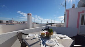 Eine Dachterrasse mit einem Tisch für zwei Personen, ausgestattet mit einer weißen Tischdecke, Tellern, Besteck und einer Obstschale.