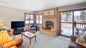 Een gezellige woonkamer met een stenen open haard, een televisie, lederen meubels en uitzicht op een besneeuwd terras.