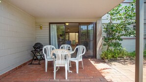 Un patio con mesa y sillas, una parrilla de barbacoa y una puerta corrediza de vidrio que da a un espacio interior.