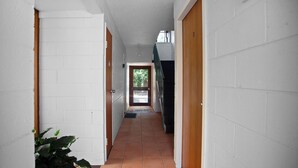 Un pasillo estrecho con paredes de ladrillo blanco, una puerta de madera al final y suelo de baldosas.