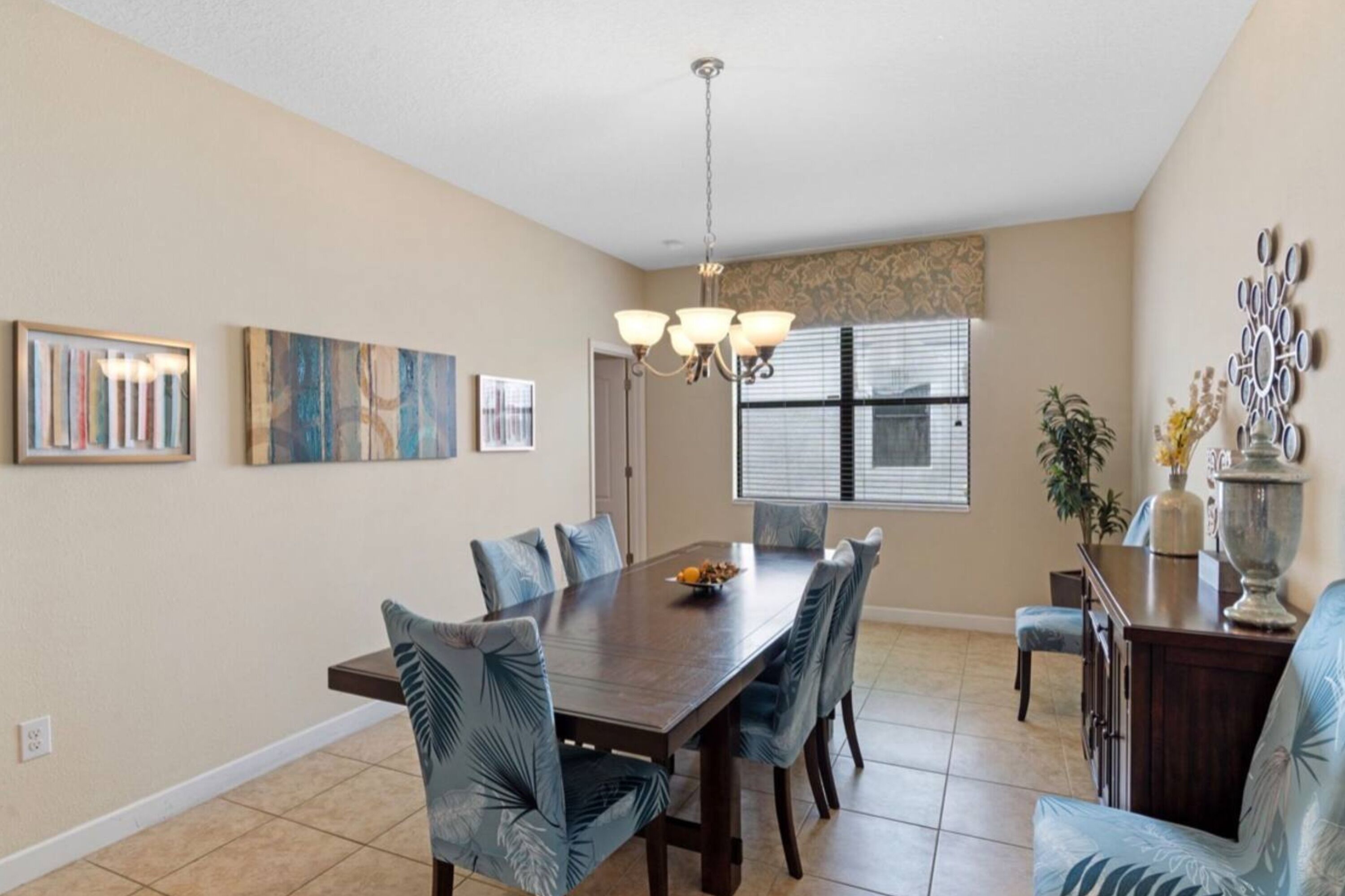 A dining area with a wooden table and matching chairs, a chandelier, and artwork on the walls.