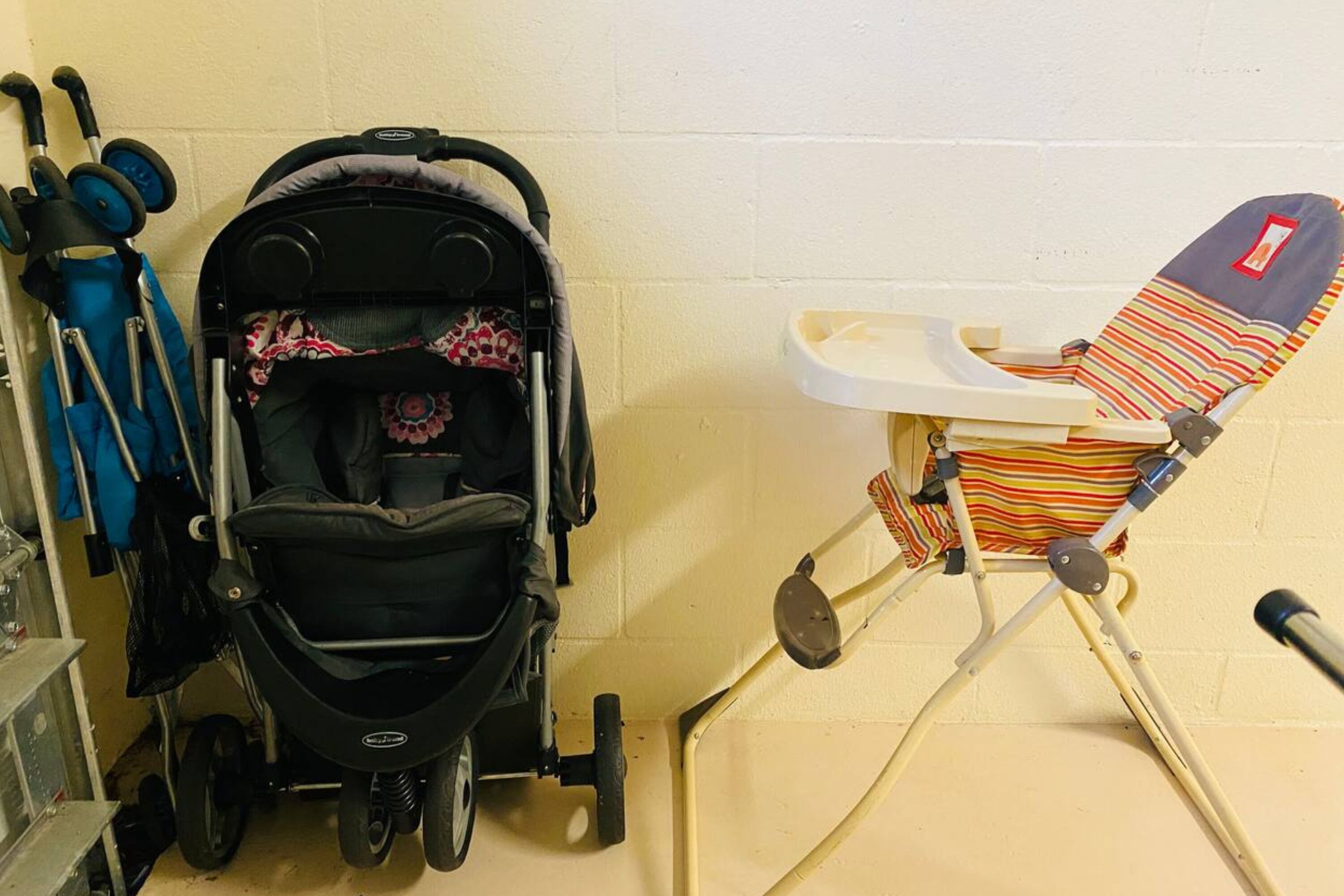 A room with a stroller and a high chair against a wall.
