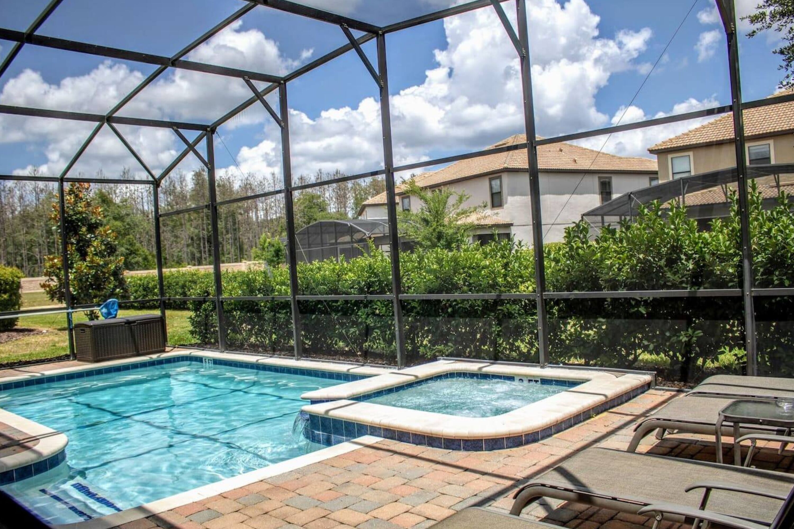 A backyard pool with two hot tubs, surrounded by a metal fence, and a view of houses in the background.