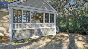 En overdækket veranda med en espalier-gelænder, et lille verandaområde og udsigt til de omkringliggende træer.