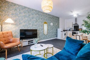 A modern living room with a sofa, TV, and a dining area with chairs and a table. - Manchester Apartment Free Parking (Salford)