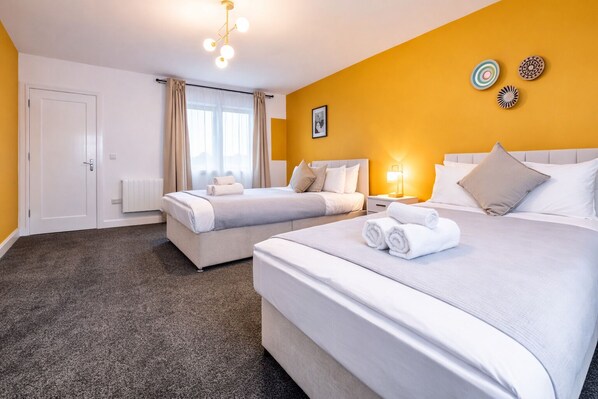 A hotel room with two beds, a window with curtains, a radiator, and a wall with decorative plates. - Manchester Apartment Free Parking (Salford)