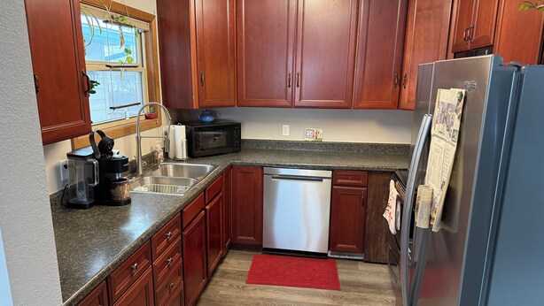 A kitchen with wooden cabinets, a stainless steel refrigerator, a dishwasher, a coffee maker, and a microwave.