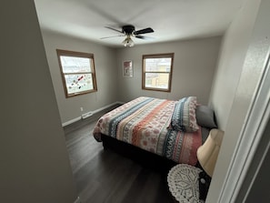 Un dormitorio con una cama, ventilador de techo, dos ventanas y una puerta.