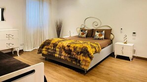 A modern bedroom with a bed, bedside tables, a dresser, and a window with curtains. - Valletta Harbour View - Grand (Sliema)