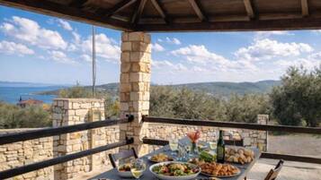 An outdoor dining area with a stone table and chairs, set against a scenic backdrop of hills and a clear sky.