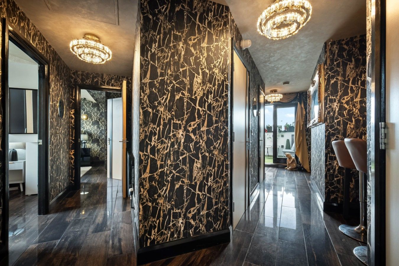 A modern hallway with marble walls and a reflective floor, leading to a room with a bed and a window.