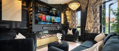 A modern living room with a large flat-screen TV, comfortable seating, and a decorative chandelier.
