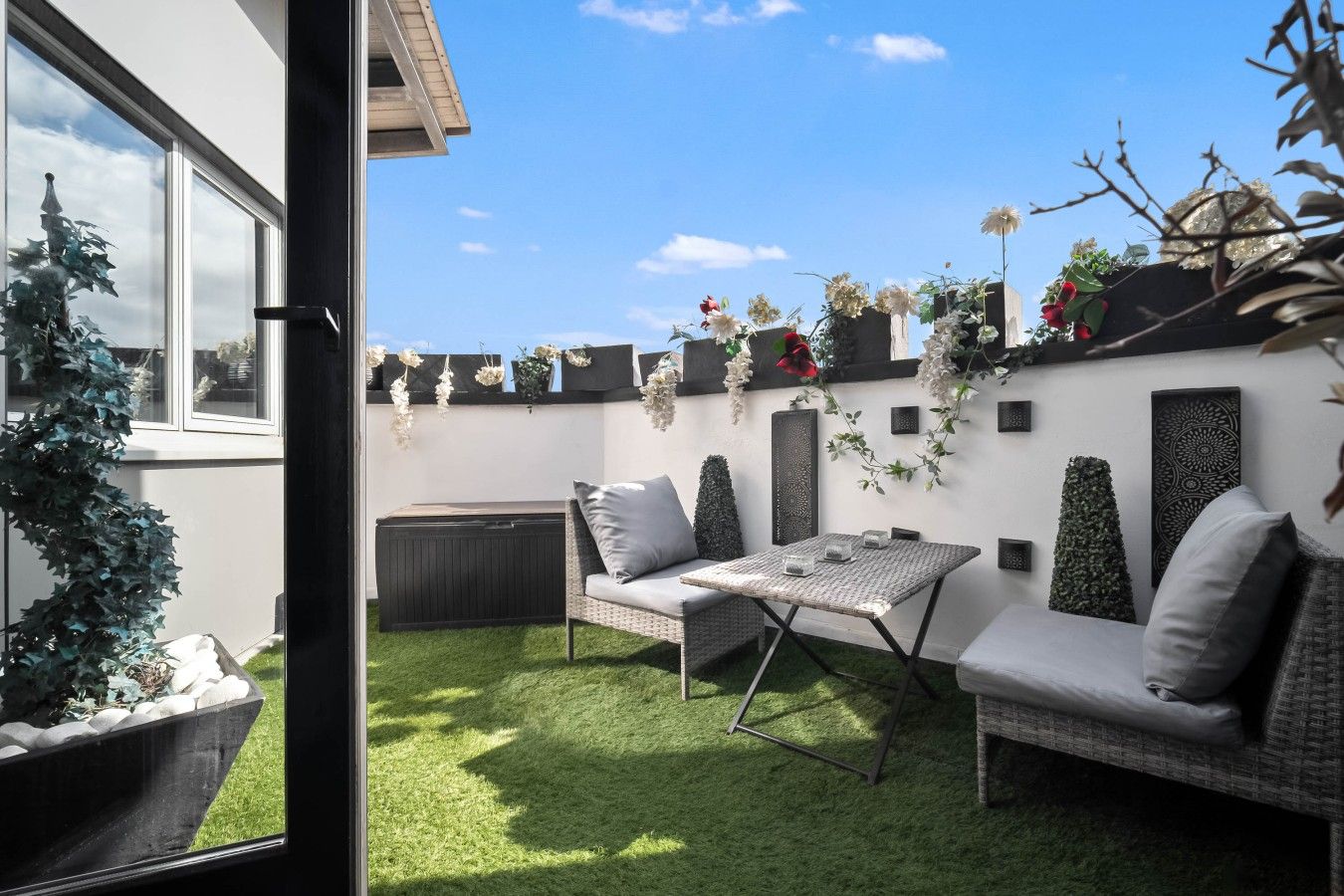 En terrasse med et bord og to sofaer, omgivet af grøn vegetation og prydplanter.