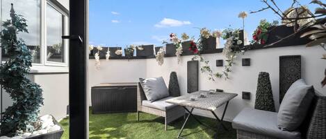 A patio with a table and two sofas, surrounded by greenery and decorative plants.