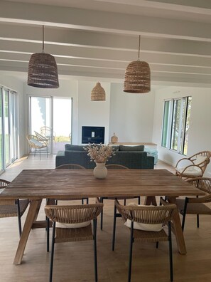 Een ruime woonkamer met een grote houten eettafel, omringd door rieten stoelen, een bank en een flatscreen televisie.
