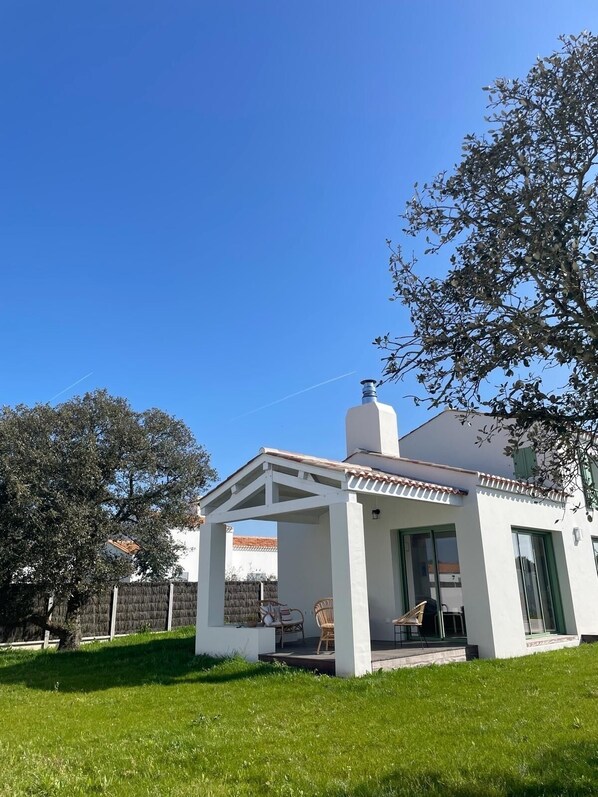 Een modern wit huis met een overdekt terras, een schoorsteen en een verzorgd gazon.