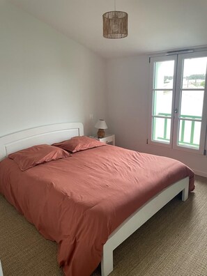 Een slaapkamer met een bed, nachtkastje, lamp en een raam met uitzicht.