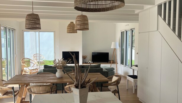 Een moderne keuken met een marmeren eiland, rieten hanglampen en een eethoek met rieten stoelen en een houten tafel.