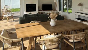 Een ruime woonkamer met een grote houten tafel, rieten stoelen, een groene bank en een piano.