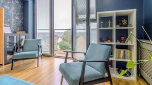 Ein modernes Wohnzimmer mit zwei Sesseln, einem Bücherregal und Blick durch ein großes Fenster.