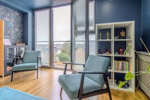 Ein modernes Wohnzimmer mit zwei Sesseln, einem Bücherregal und Blick durch ein großes Fenster.