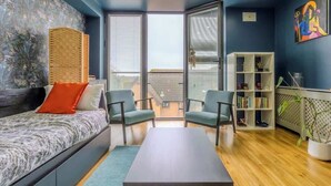 Ein modernes Zimmer mit einem Bett, zwei Stühlen, einem Tisch, einem Bücherregal und einem großen Fenster.