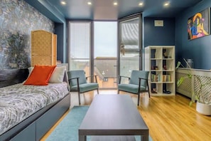 Ein modernes Zimmer mit einem Bett, zwei Stühlen, einem Tisch, einem Bücherregal und einem großen Fenster.