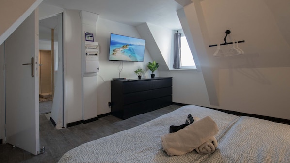 Ein Schlafzimmer mit Bett, Kommode, Fernseher und Fenster mit Blick auf einen Strand.