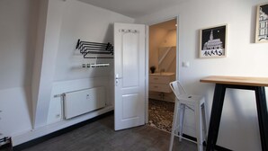 A room with a white door, a radiator, a white chair, a small table, and a framed picture on the wall.