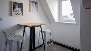 A small room with a sloped ceiling, a table with a wooden top, two white chairs, and two framed pictures on the wall.