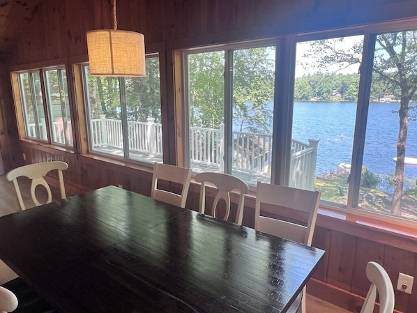 A room with a large dark wooden table and white chairs, large windows with a view of a lake and deck. - NEW: Lakefront Cottage on Kennebunk Pond, sleeps 6 (Lyman)