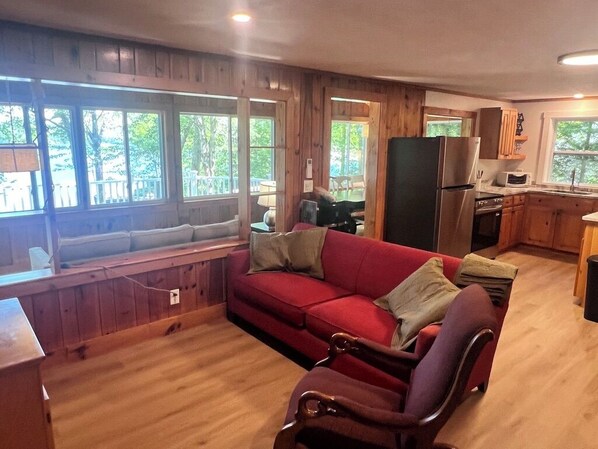 A cozy living room with a red sofa, a wooden bench, and a dining area with a refrigerator and microwave.